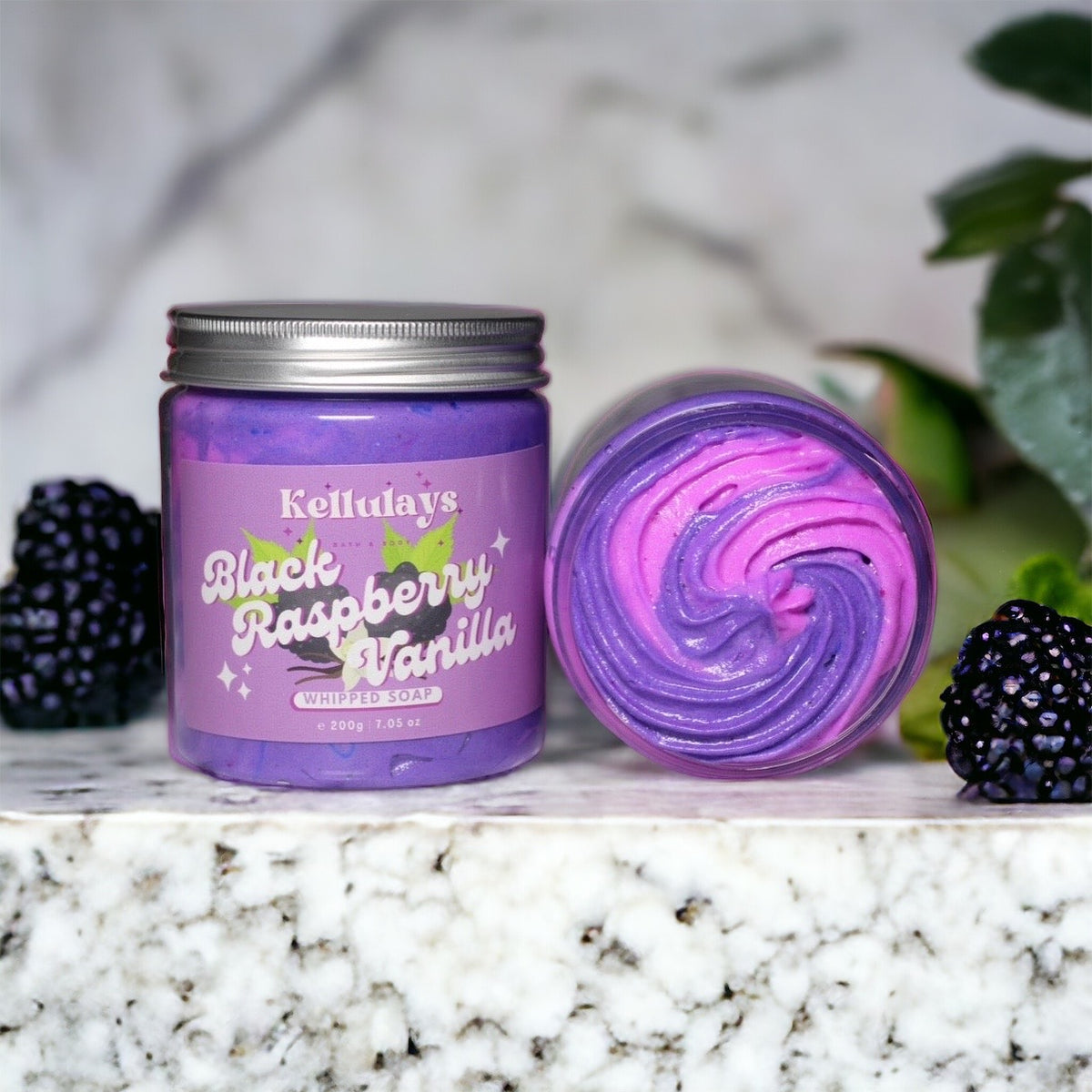 Close-up of a jar of Kellulays Black Raspberry and Vanilla Whipped Soap, featuring a swirling blend of light purple and dark purple. This handmade bath whip has a silky texture and is enriched with nourishing cocoa and shea butters, designed to cleanse, moisturize, and rejuvenate the skin. The label on the jar highlights the luxurious scent of black raspberry and vanilla.