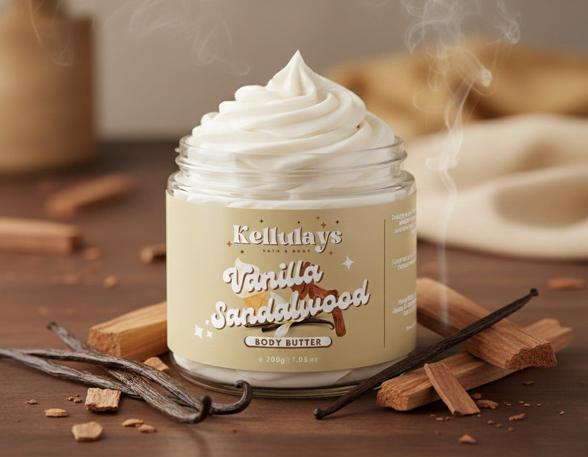 A jar of Kellulays Vanilla Sandalwood Whipped Body Butter sitting on a wooden surface, filled with a thick, creamy white swirl. Te beige label features the Kellulays logo and product name. Surrounding the jar are vanilla bean pods and sandalwood pieces, with soft steam rising in the background for a warm, cosy, dessert-like atmosphere.
